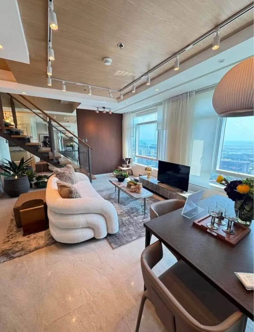 Seen from the dining table, the staircase rises behind the living area beside tall windows