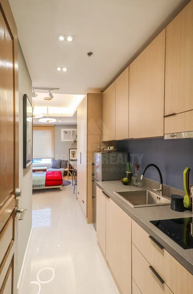 A galley kitchen with wood-finish cabinets runs from the door toward the living area